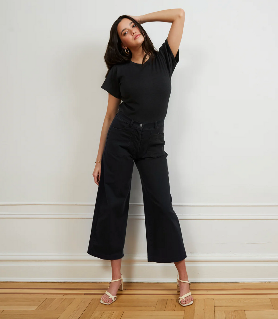 Woman wearing a black outfit standing against a white wall.